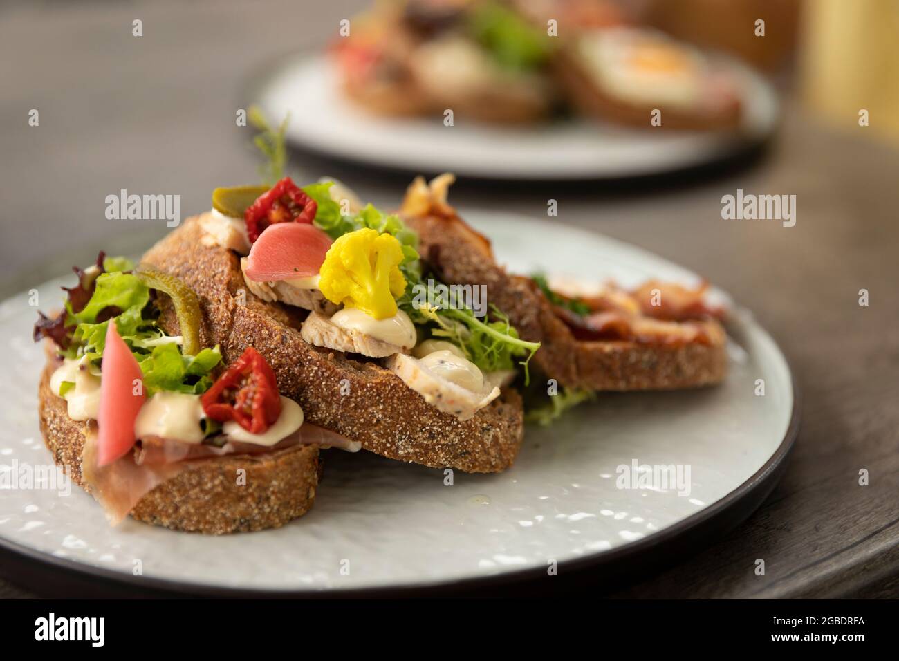Piatto di panino club sano fatto in casa con ingredienti freschi come pomodoro, insalata, lattuga, pancetta, cavolfiore e pollo su un rustico pane marrone beau Foto Stock