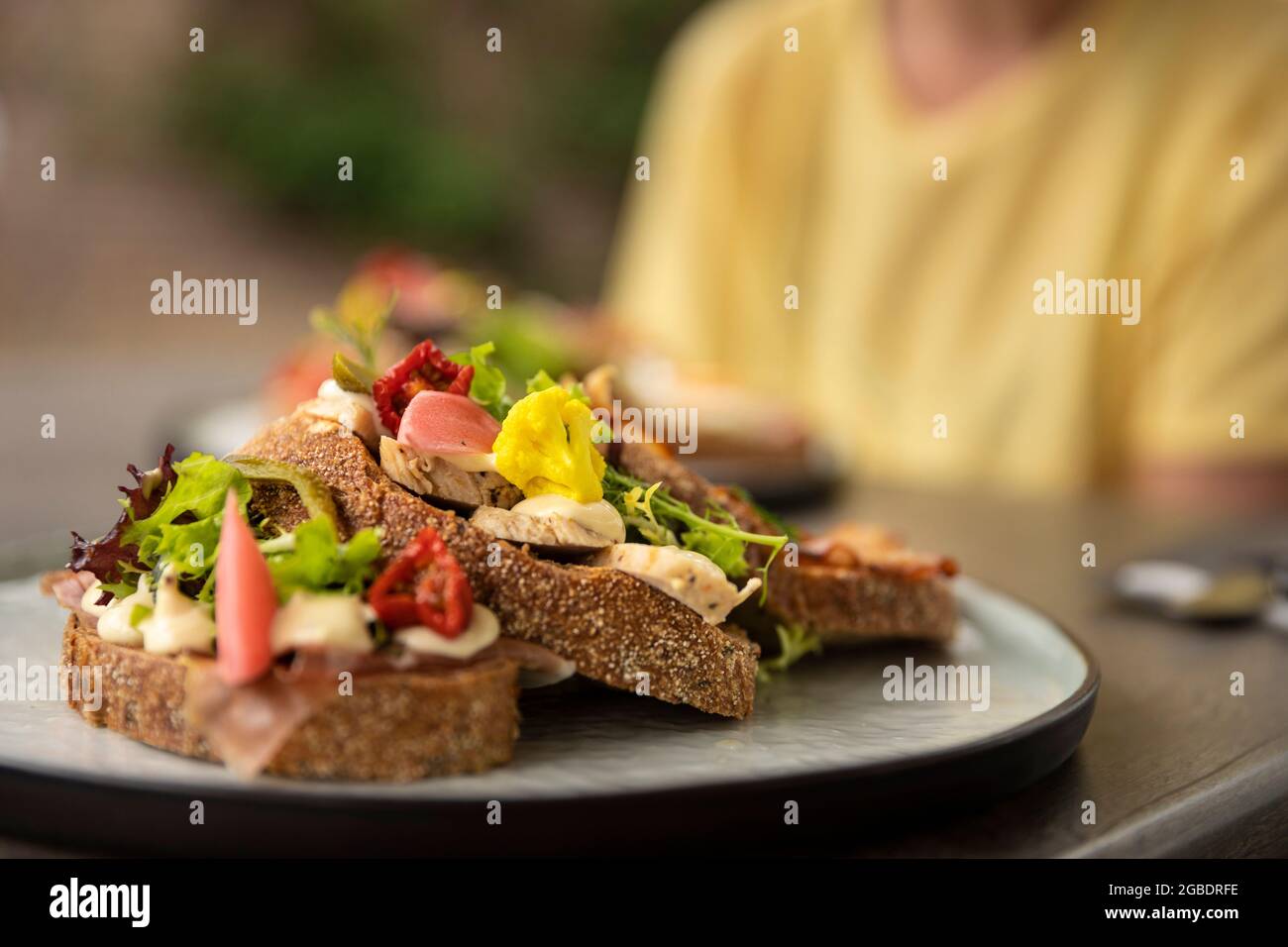 Sano sandwich fatto in casa club con ingredienti freschi come pomodoro, insalata, lattuga, pancetta, cavolfiore e pollo su fette di pane marrone rustico b Foto Stock