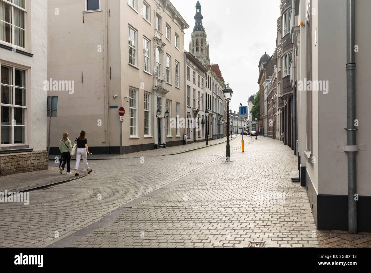 Breda, Paesi Bassi 28 giugno 2021. Strada nel centro della città con vecchi edifici storici con facciate chiare, un marciapiede, una chiesa e persone wal Foto Stock