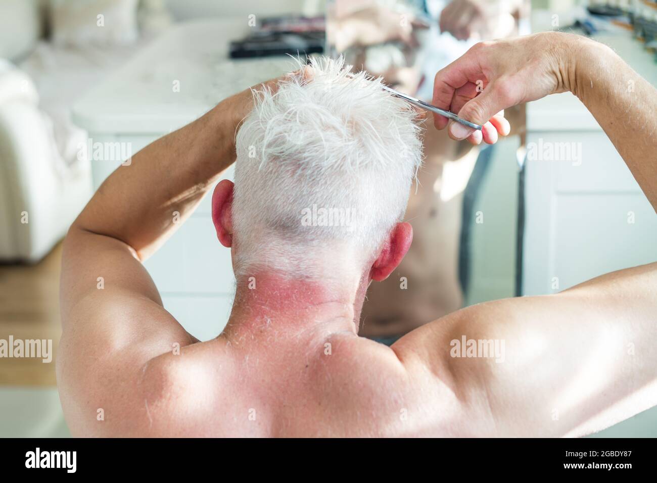 Vista posteriore l'uomo bianco dei capelli che fa il taglio auto con le forbici e guarda nello specchio. Self-care a casa nelle condizioni di quarantena globale e chiuso Foto Stock