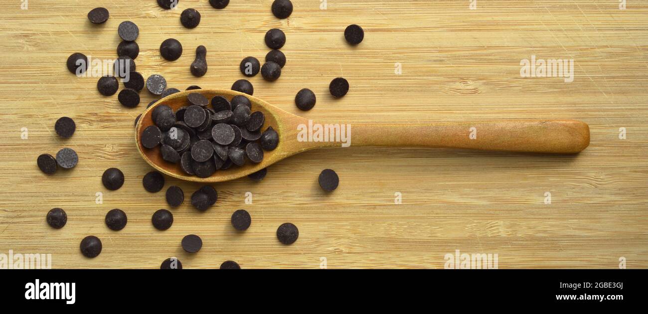 Deliziose gocce di cioccolato fondente in cucchiaio di legno, sul tagliere  Foto stock - Alamy