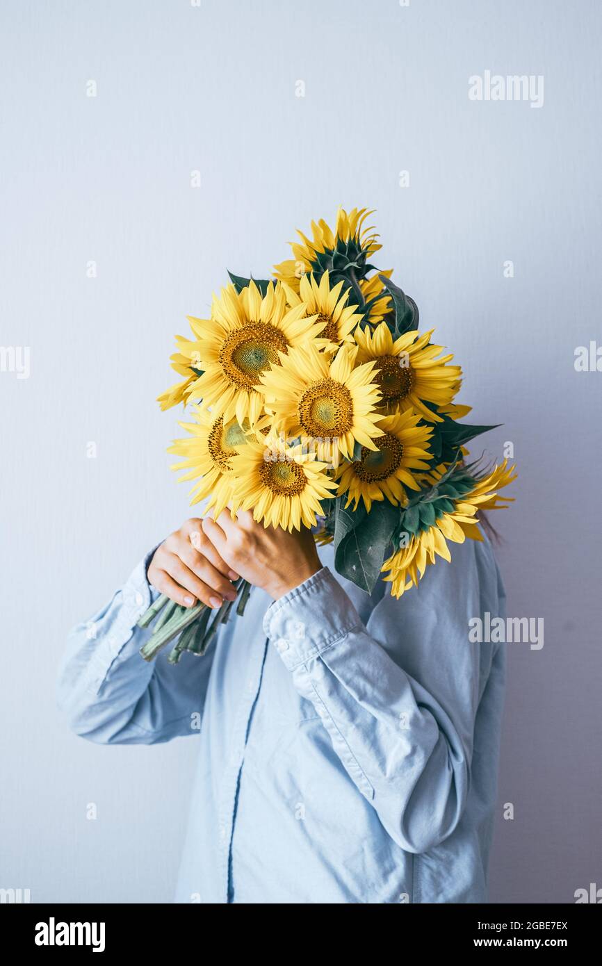 Giovane bella donna che tiene un bouquet di girasoli su uno sfondo bianco. Composizione floreale minima. Foto di alta qualità Foto Stock