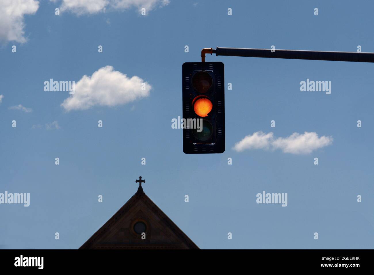 Un semaforo giallo con una chiesa e croce sullo sfondo a Santa Fe, New Mexico. Foto Stock