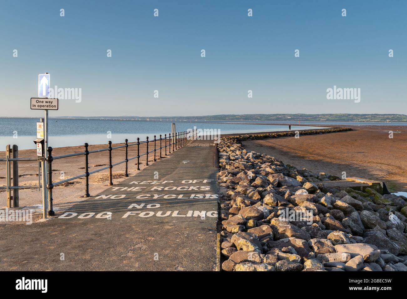 West Kirby, Wirral, Regno Unito. Percorso lungo il perimetro del lago marino con un cartello di sola andata e avviso per tenere fuori le rocce. Foto Stock