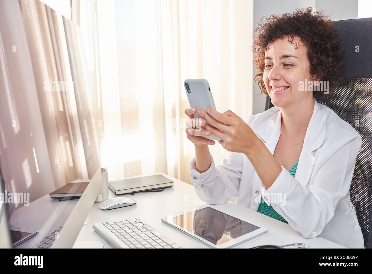 Una dottoressa che usa il suo smartphone sul posto di lavoro Foto Stock