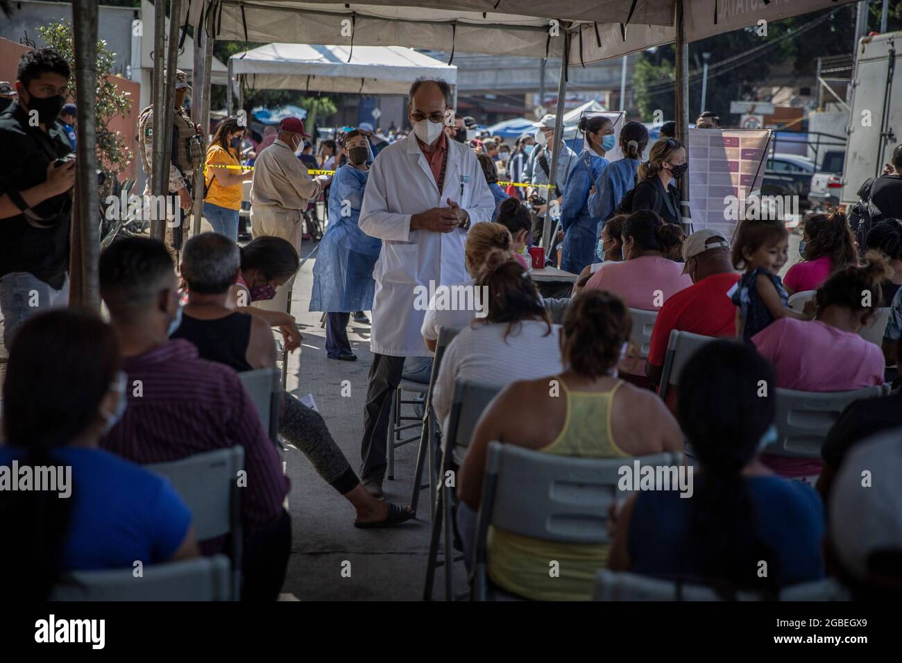 Tijuana, Messico. 3 agosto 2021. Un medico che copre la bocca e il naso osserva i migranti che hanno ricevuto una vaccinazione a Corona al confine con El Chaparral. La campagna di vaccinazione è stata organizzata dal dipartimento sanitario dello stato messicano di Baja California. Circa 500 migranti che vivevano nel campo improvvisato al valico di frontiera dovevano ricevere il vaccino Corona da Pfizer-Biontech. Credit: Stringer/dpa/Alamy Live News Foto Stock