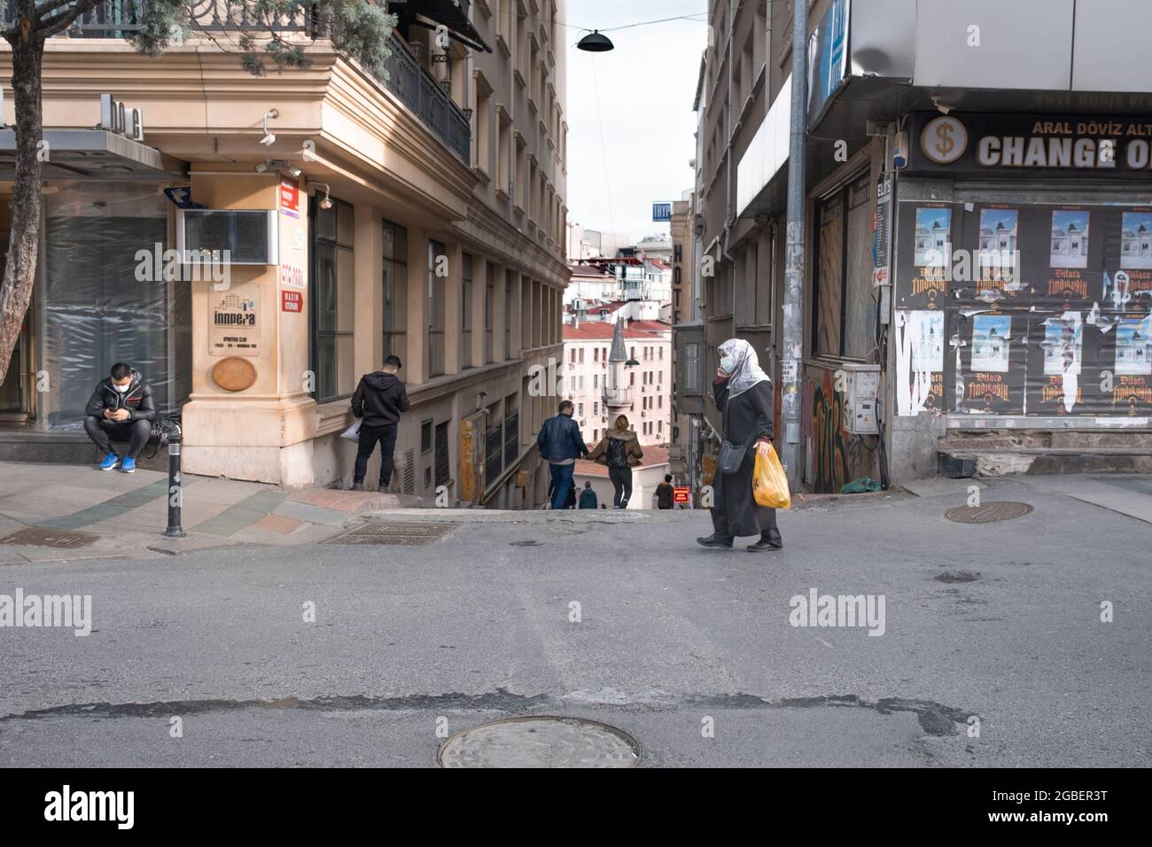 Beyoglu, Istanbul, Turchia - 02.17.2021: Persone con mascherine covid protezione camminare in via Taksim Siraselviler in una giornata invernale e moschea sembra essere Foto Stock