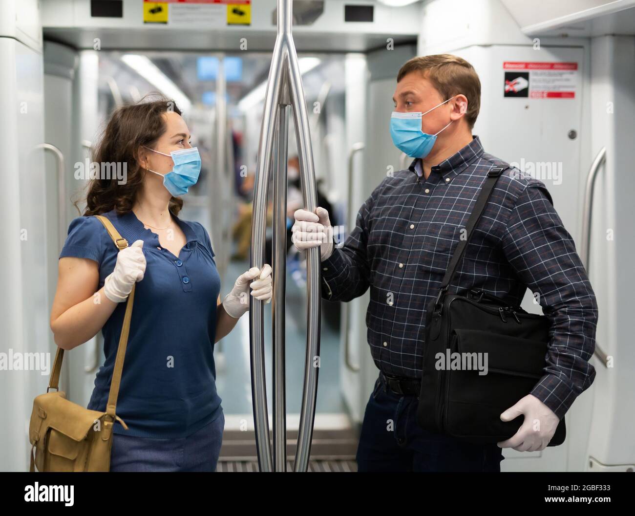 Uomo e donna in maschere mediche che chiacchierano in auto metropolitana Foto Stock