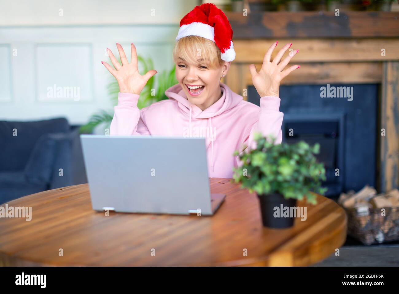 Foto di felice giovane donna emozionata a Santa Hat davanti al monitor del computer portatile. Incontro online con amici o familiari alla vigilia di Natale o Capodanno. Foto Stock