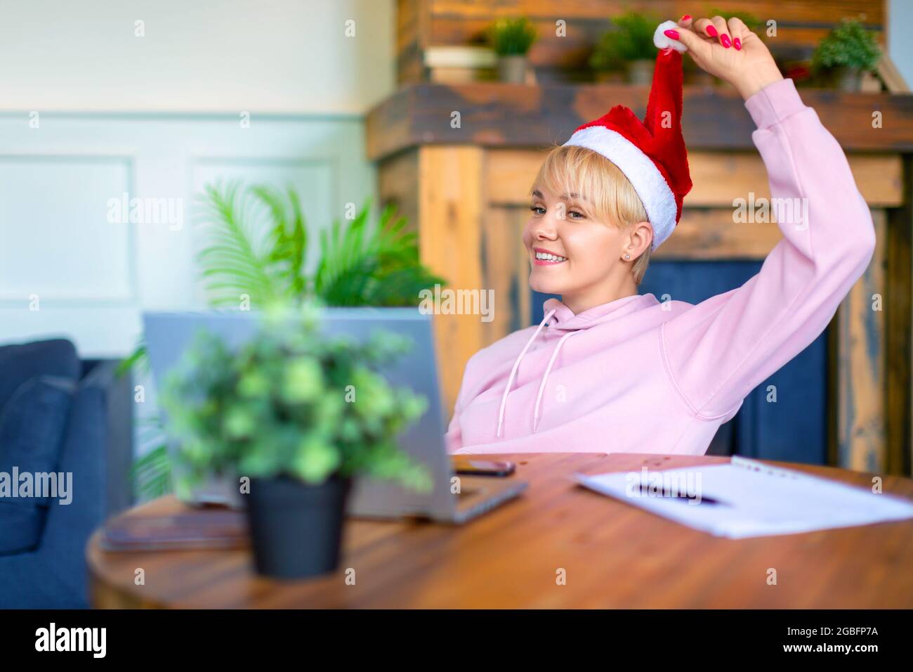 Foto di una giovane donna in un cappello di Santa davanti a un monitor per computer portatile in casa. Incontro online con amici o parenti alla vigilia di Natale Foto Stock