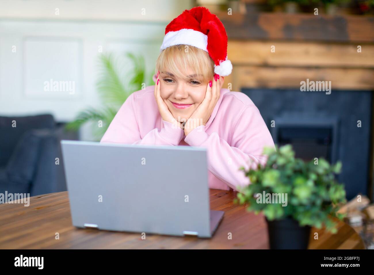 Felice giovane donna sorridente nel cappello di Santa davanti al monitor del laptop. Incontro online con amici o familiari alla vigilia di Natale o Capodanno. Foto Stock