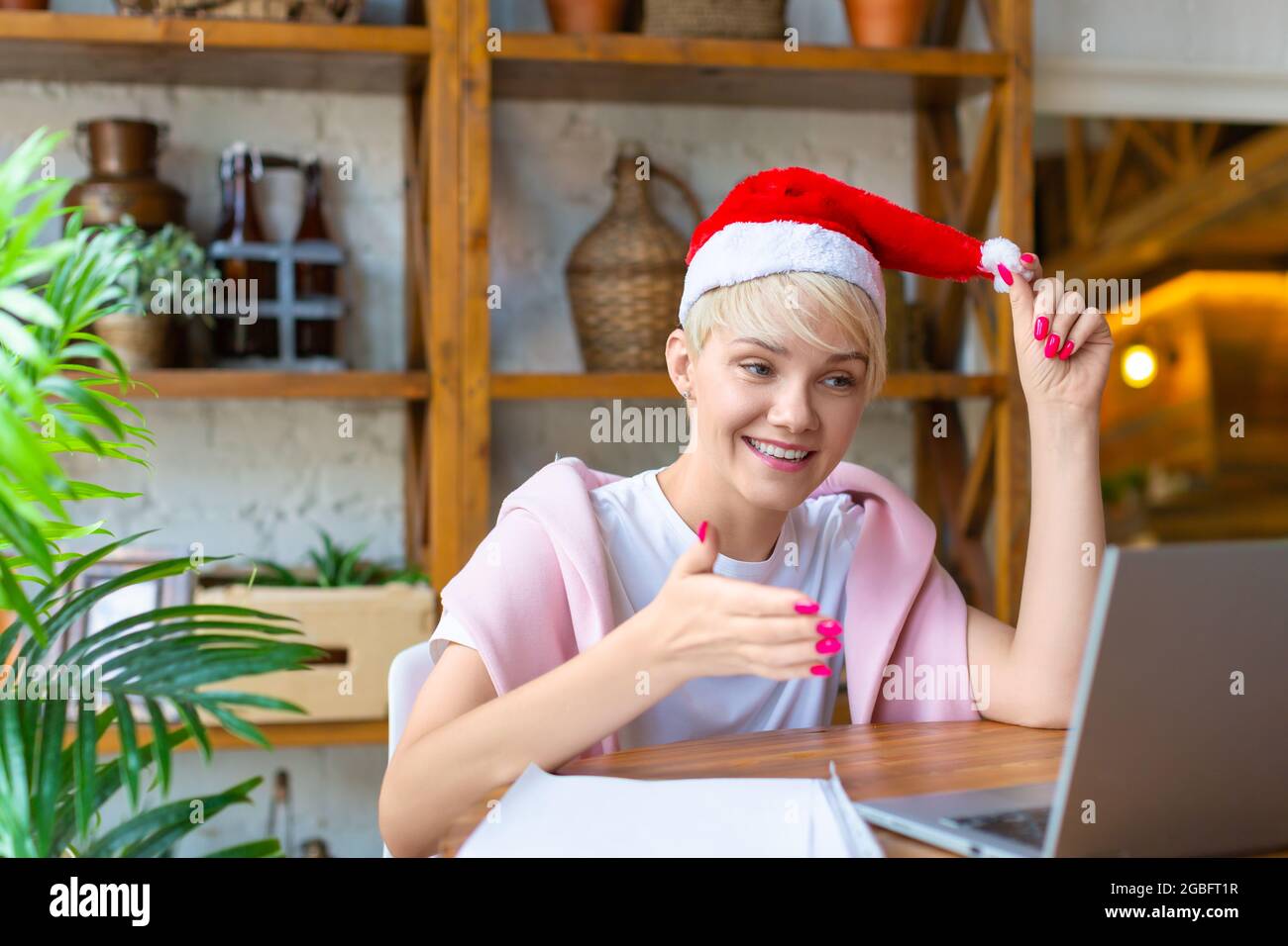Foto di felice giovane donna emozionata a Santa Hat davanti al monitor del computer portatile. Incontro online con amici o familiari alla vigilia di Natale o Capodanno. Foto Stock
