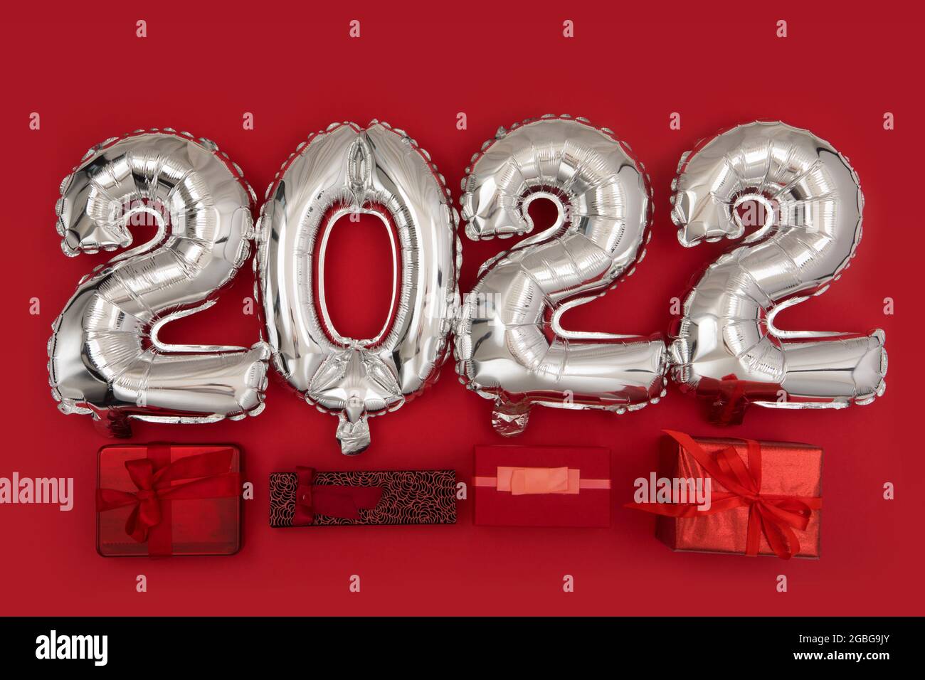 Vista dall'alto del set di regali avvolti posizionati vicino ai palloncini d'argento 2022 durante la celebrazione di Capodanno su sfondo rosso Foto Stock
