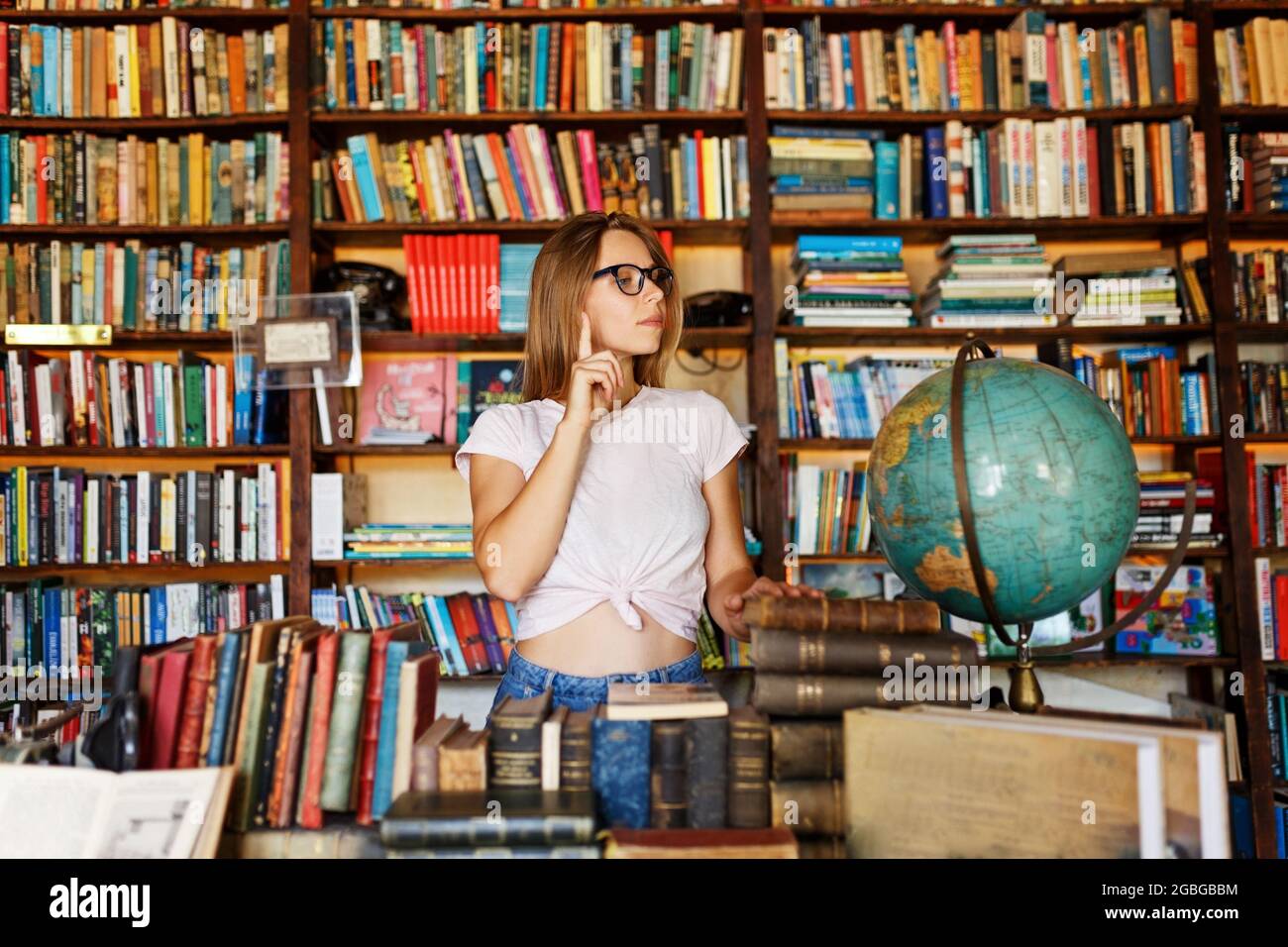 Giovane sorridente attraente ritratto di ragazza dell'università con gli occhiali in piedi in biblioteca, tenendo libri. Concetto di educazione. Foto Stock