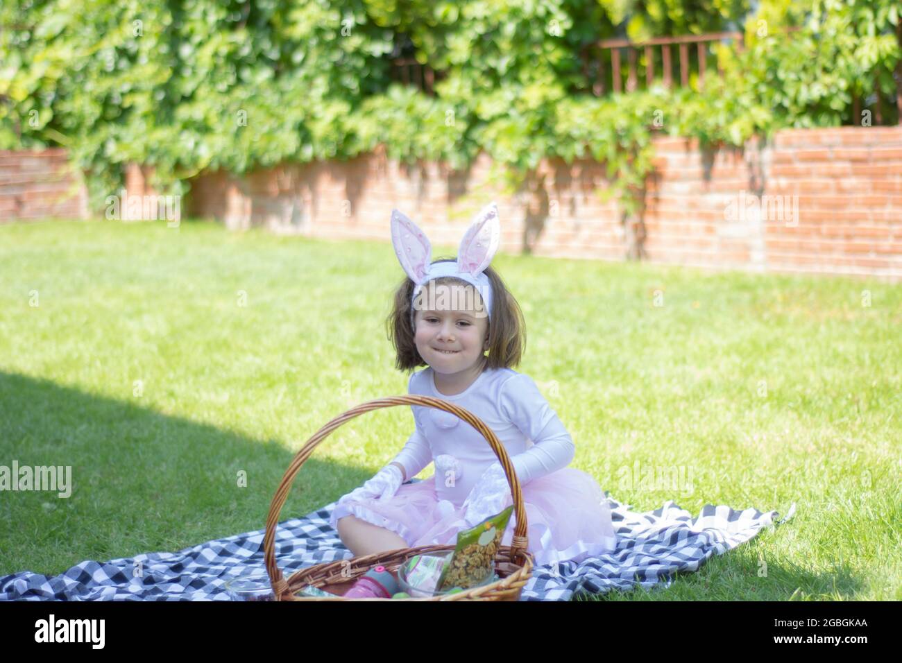 bambina in un costume coniglietto sta avendo un picnic nel giardino della sua casa. Foto Stock