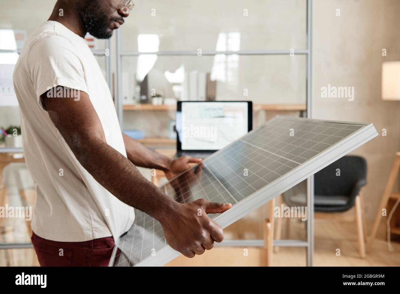 Ingegnere africano serio che tiene la batteria solare nelle sue mani durante il lavoro in ufficio Foto Stock