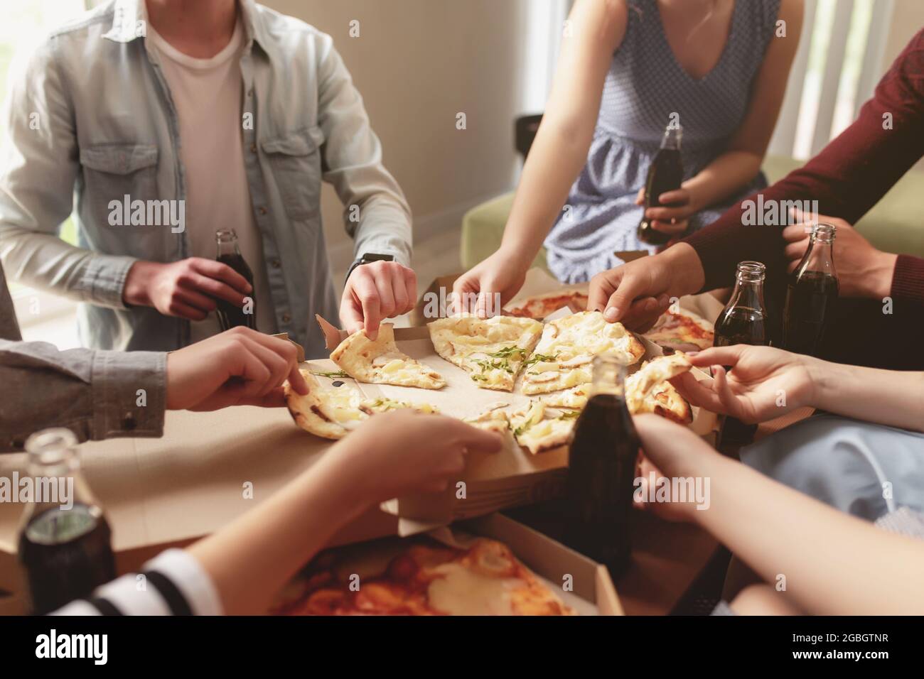 Una pizza party, un gruppo di amici che chiacchierano e mangiavano felicemente la pizza al tavolo e bevono acqua dolce. Molti amici che si tramandano insieme beca Foto Stock