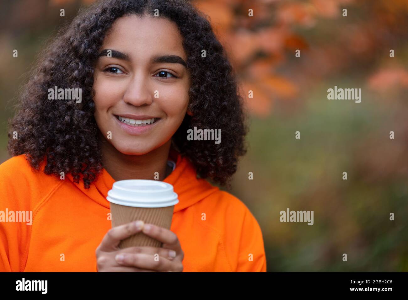 Bella felice mista razza Africana americana ragazza adolescente femmina giovane donna indossando una felpa con cappuccio arancione sorridente bere togliere il caffè fuori durante Foto Stock