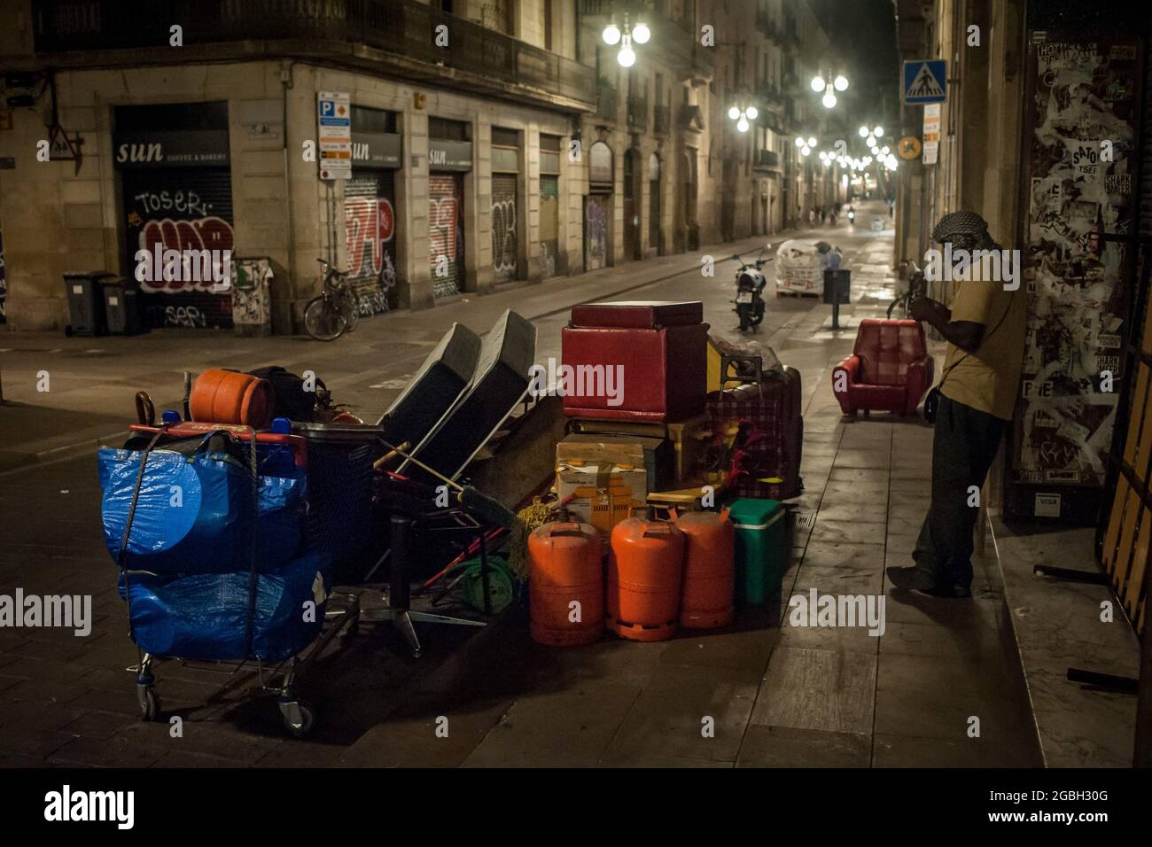 Durante il coprifuoco di notte un commerciante di rottami attende accanto ai mobili abbandonati su una strada della città vecchia di Barcellona. Foto Stock