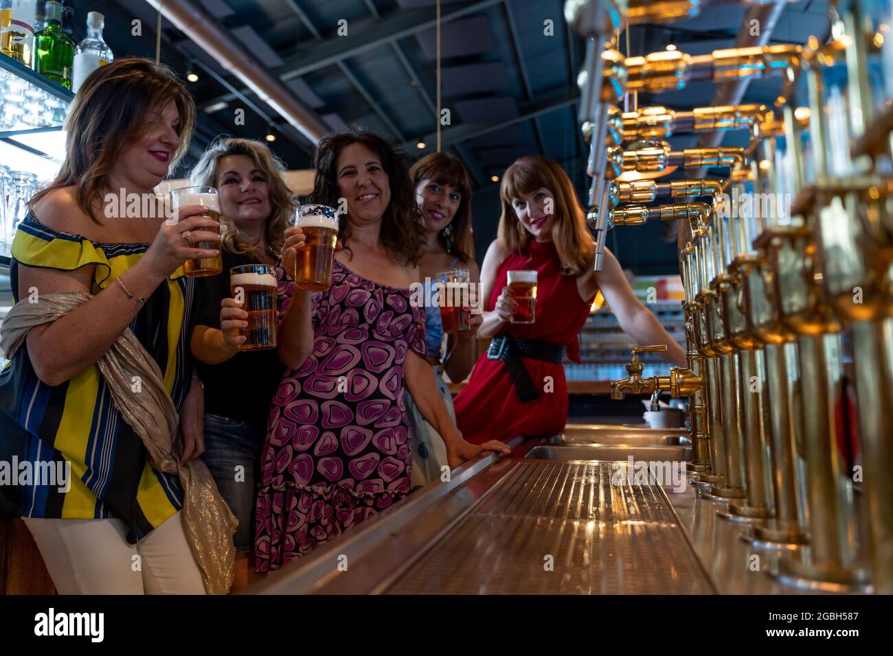 un gruppo di donne mature sorridenti beve birra in un pub di fronte a una presa di birra Foto Stock
