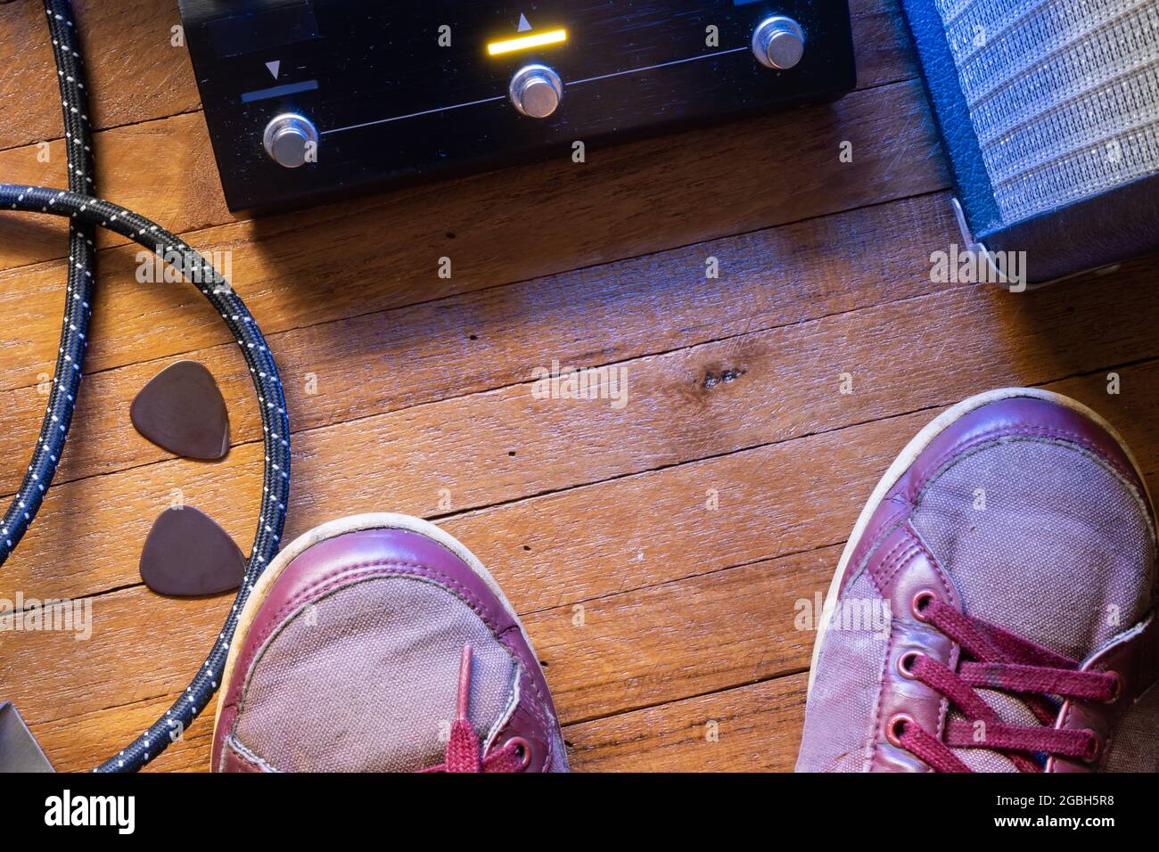 Il punto di vista del chitarrista sul palco. Pedale di chitarra, cavo, chitarra, amplificatore e scarpe su pavimento in legno. Foto Stock