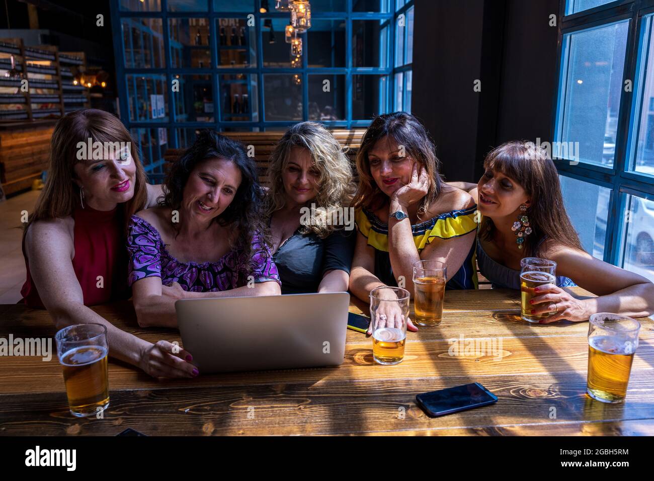 gruppo di belle amiche che si divertono bevendo birra e guardando il computer in un pub Foto Stock