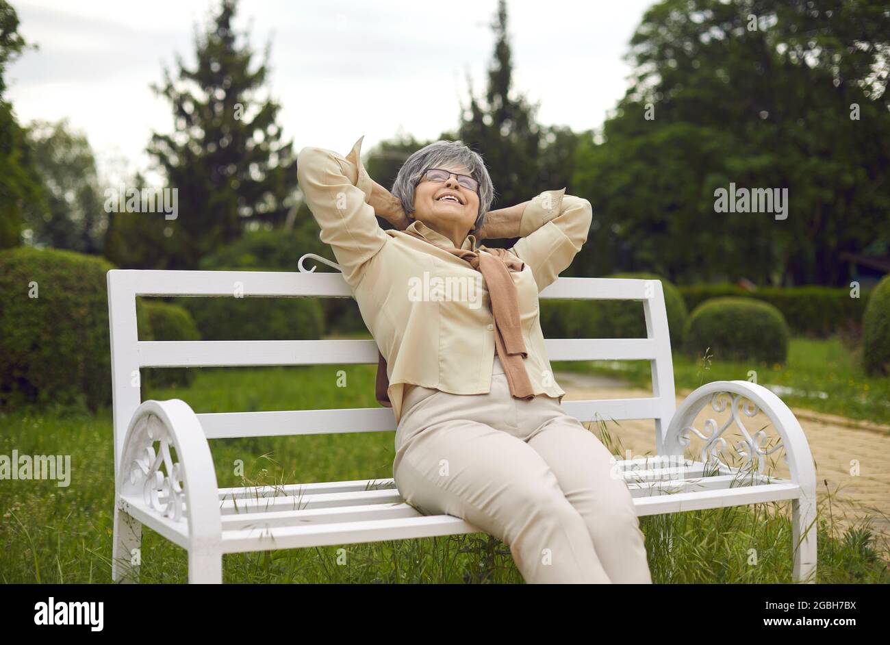 Felice delizia anziana donna con capelli grigi che guarda in su seduta sulla panchina nel parco Foto Stock