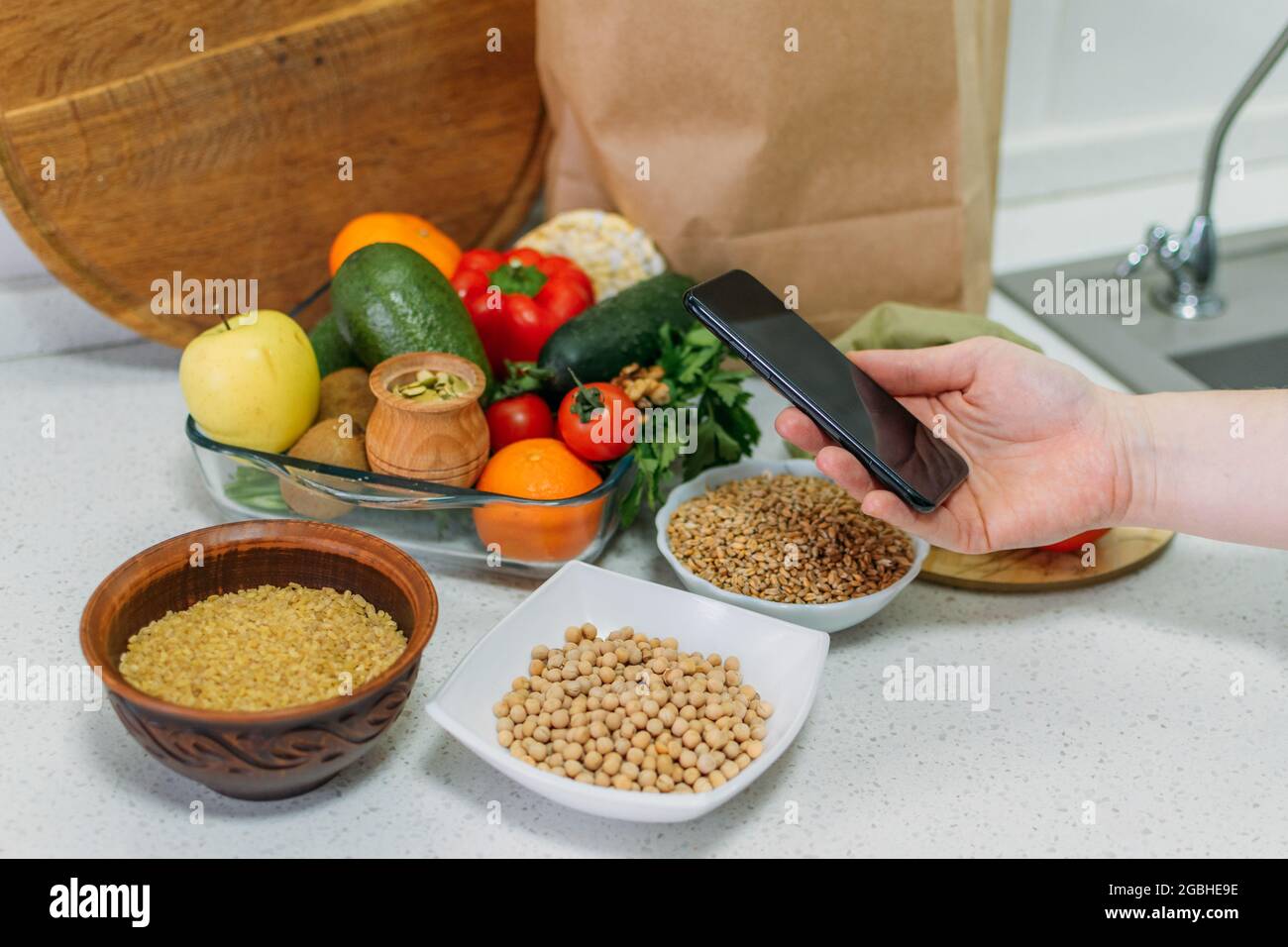 Dieta a base di piante e cibo intero per migliorare la salute. Cellulare femminile a mano con ricette a base di piante e pasto sano, verdure, frutta, cereali interi Foto Stock