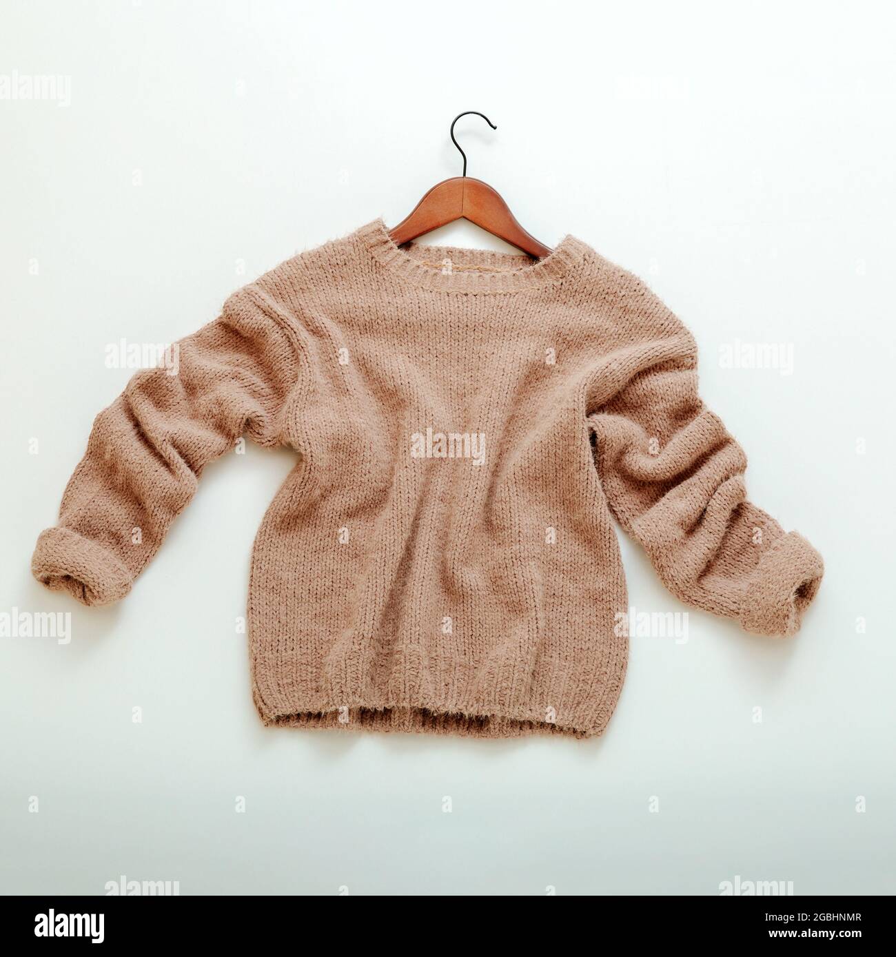 Pullover beige lavorato a maglia su appendiabiti. Il pullover in cashmere vola piatto su sfondo bianco. Caldo ed elegante abito invernale marrone caldo pullover lavorato a maglia Foto Stock