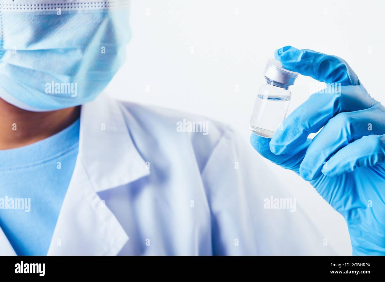 Flaconcino di closeup del vaccino covid-19 in mano a uno scienziato professionista o medico in laboratorio per il trattamento con guanti da maschera e camice da laboratorio su fondo bianco Foto Stock