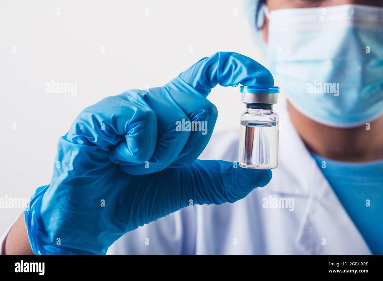 Flaconcino di closeup del vaccino covid-19 in mano a uno scienziato professionista o medico in laboratorio per il trattamento con guanti da maschera e camice da laboratorio su fondo bianco Foto Stock