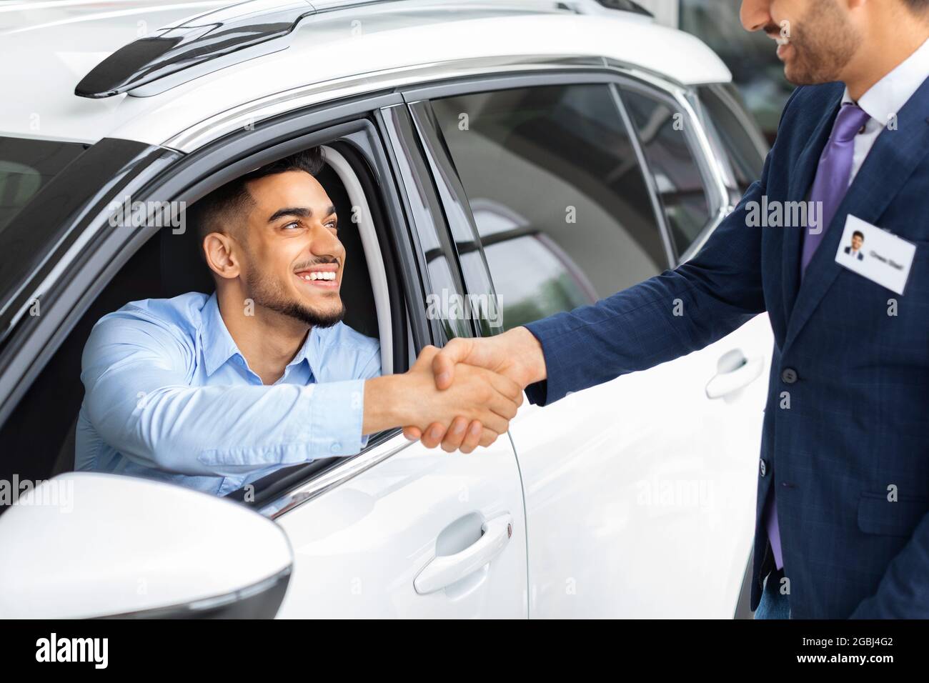 Felice uomo medio-orientale seduto in auto scuotendo mano del responsabile vendite Foto Stock