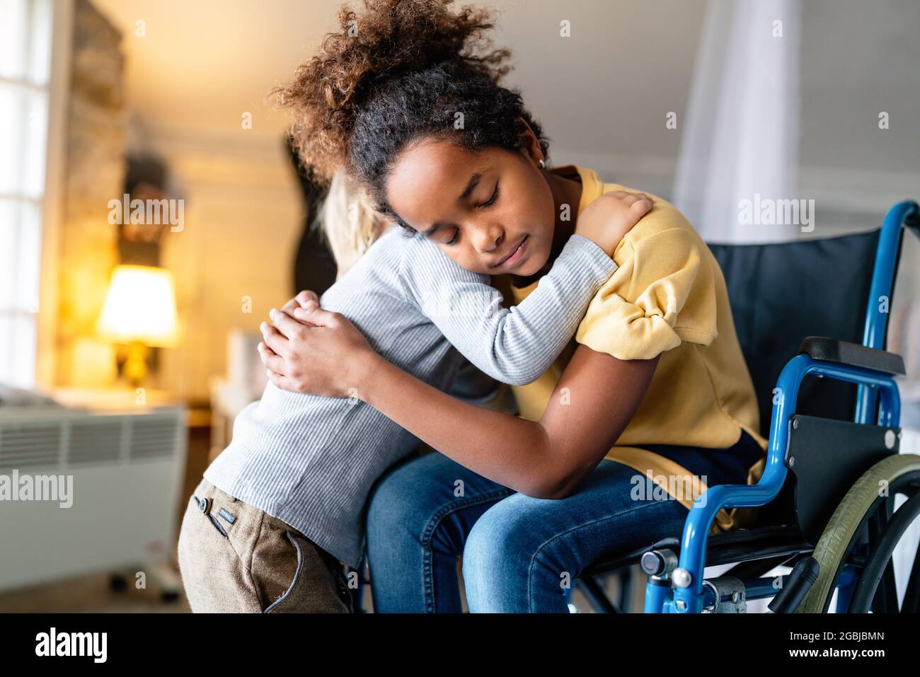 Bambina nera con disabilità in sedia a rotelle abbracciata con il fratello minore. Foto Stock