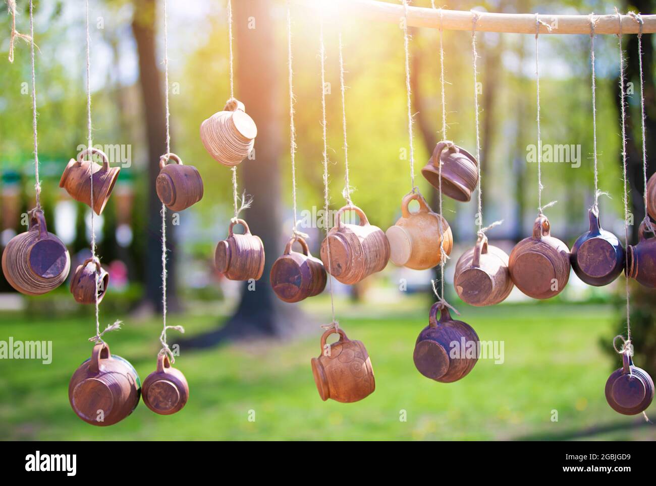 Tazze di argilla appendono dalle corde, illuminate dal sole. Vendita di prodotti artigianali di argilla. Foto Stock