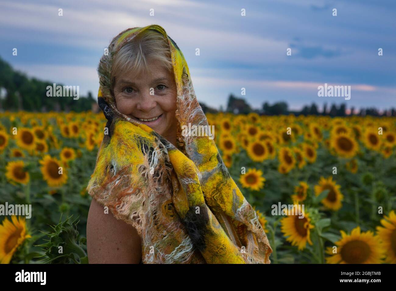 anziana bella donna in un campo di girasoli ride e gode la vita Foto Stock