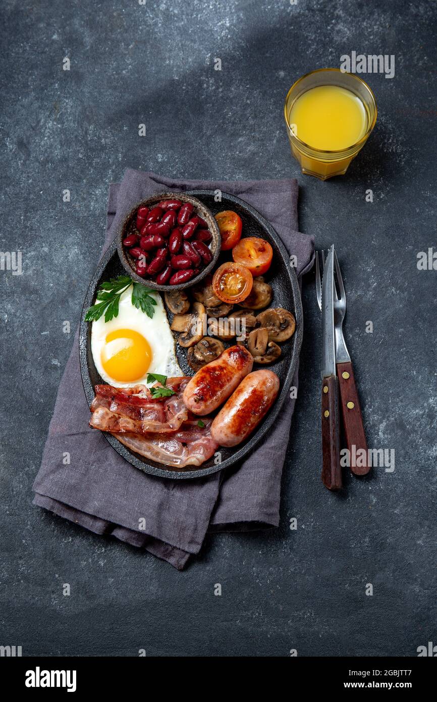 Colazione inglese con uova fritte, pancetta, salsicce, fagioli, toast su sfondo nero Foto Stock