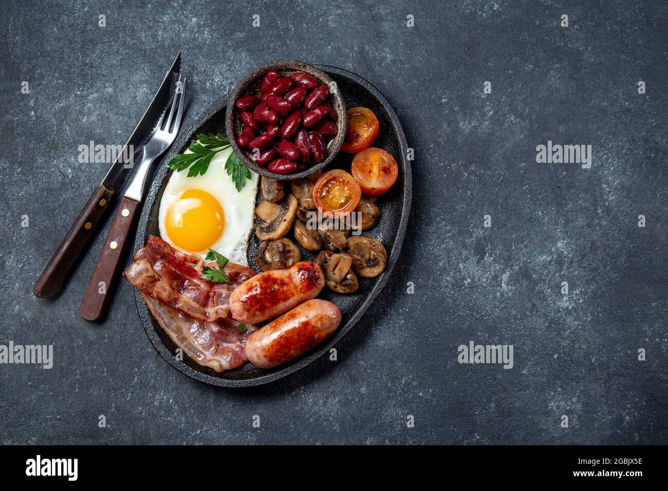 Colazione inglese con uova fritte, pancetta, salsicce, fagioli, toast su sfondo nero Foto Stock