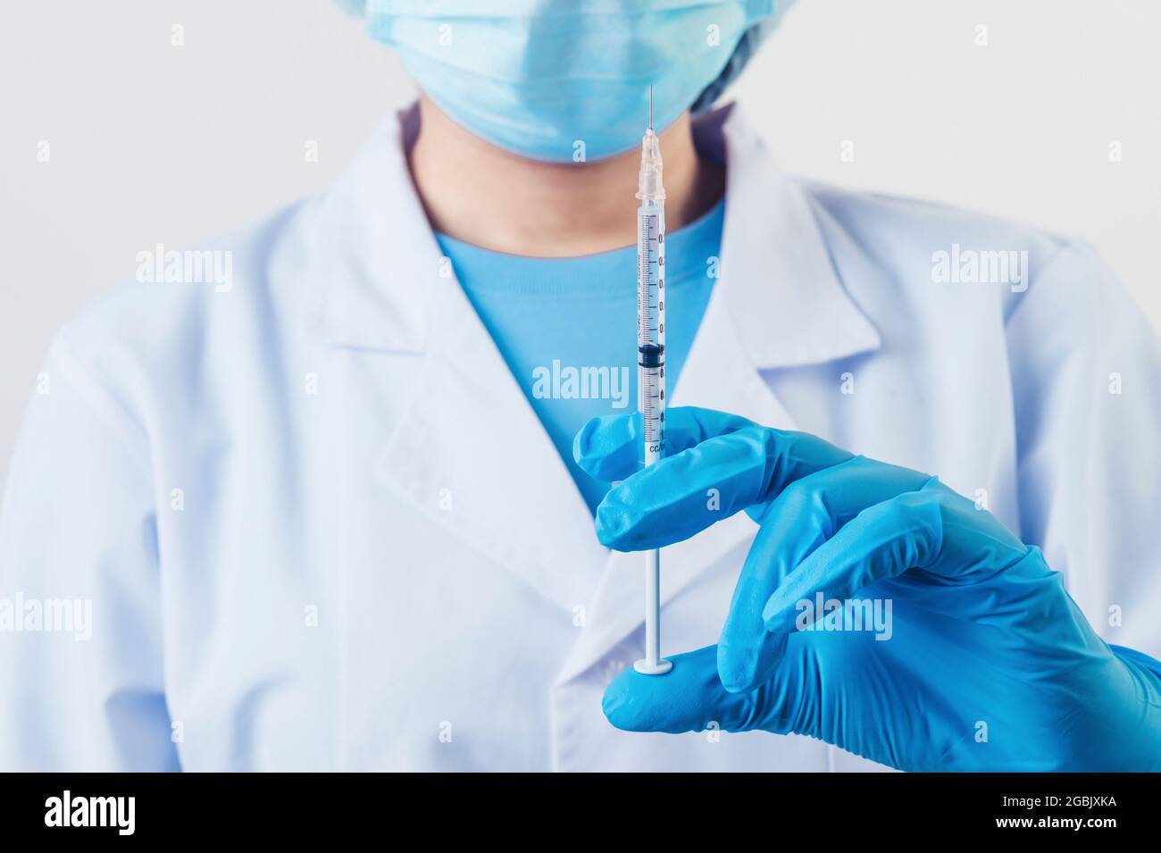 Siringa closeup ago per iniezione di vaccino covid-19 in uno scienziato professionista o medico mano in laboratorio per il trattamento con maschera guanti da laboratorio camice su bianco Foto Stock