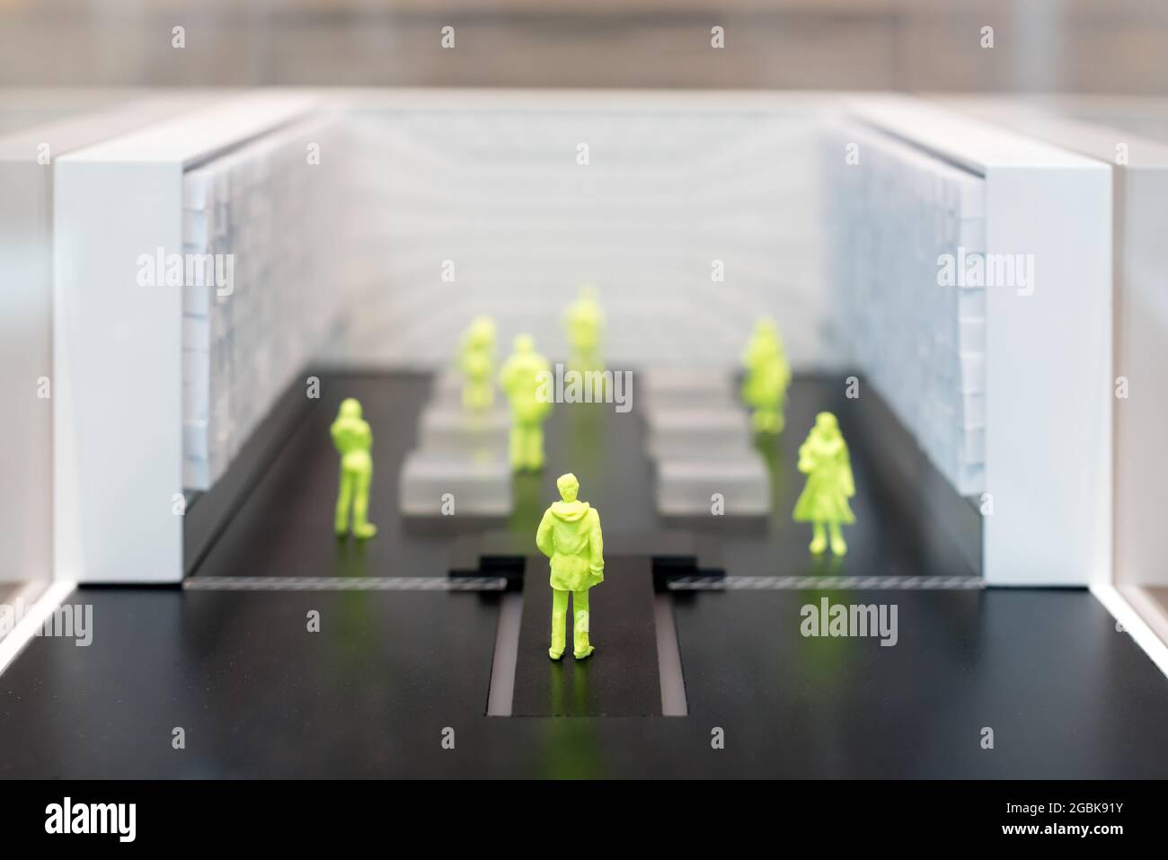 Gruppo di persone in miniatura gialla divaricare sociale in una stanza con fuoco selettivo alla parte posteriore di una figura maschile in primo piano e copyspace Foto Stock