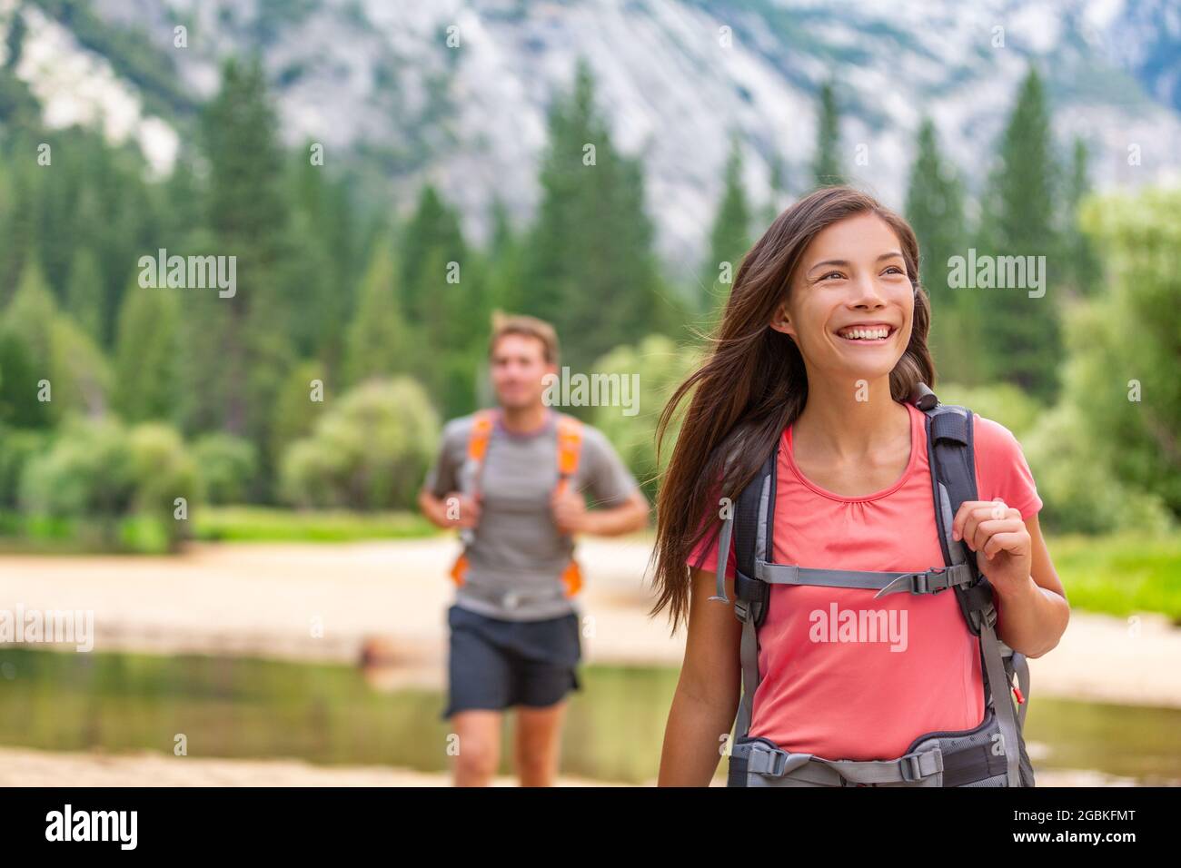 Escursionisti a piedi nella foresta naturale di Yosemite. Happy campeggiatori trekking attraverso sentieri trekking in montagna. Ragazza asiatica con zaino guardando in su, amico uomo Foto Stock