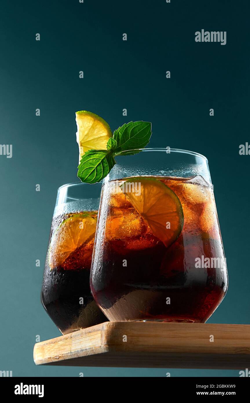 Cuba Libre o Long Island cocktail con rum, cola e lime in bicchieri su tavola di legno su sfondo blu scuro. Rinfrescante bevanda estiva. Foto Stock