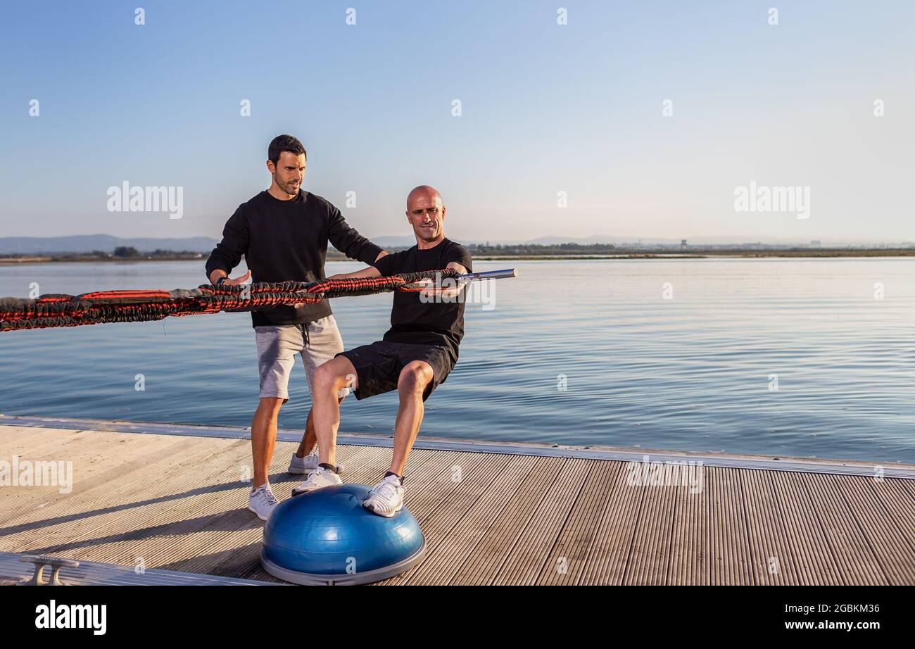 Un windsurfer su una sfera di stabilizzazione stimola la guida su una tavola con espansori di gomma. Sviluppare equilibrio e stabilità. Foto Stock
