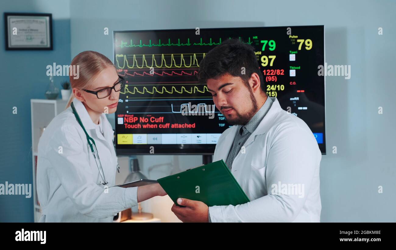 Il primo piano centrale di diversi scienziati sportivi che parlano dei risultati dei test di stress degli atleti e dei dati di EKG è stato mostrato in grande esposizione in background. Foto Stock