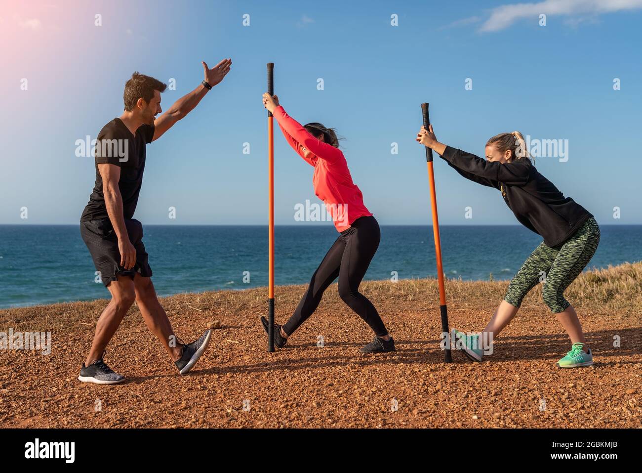 Un uomo e una donna di mezza età in una classe di fitness. Scaldare e fare esercizio sulla riva dell'oceano. Utilizzo di bastoncini da ginnastica per l'allungamento. Foto Stock