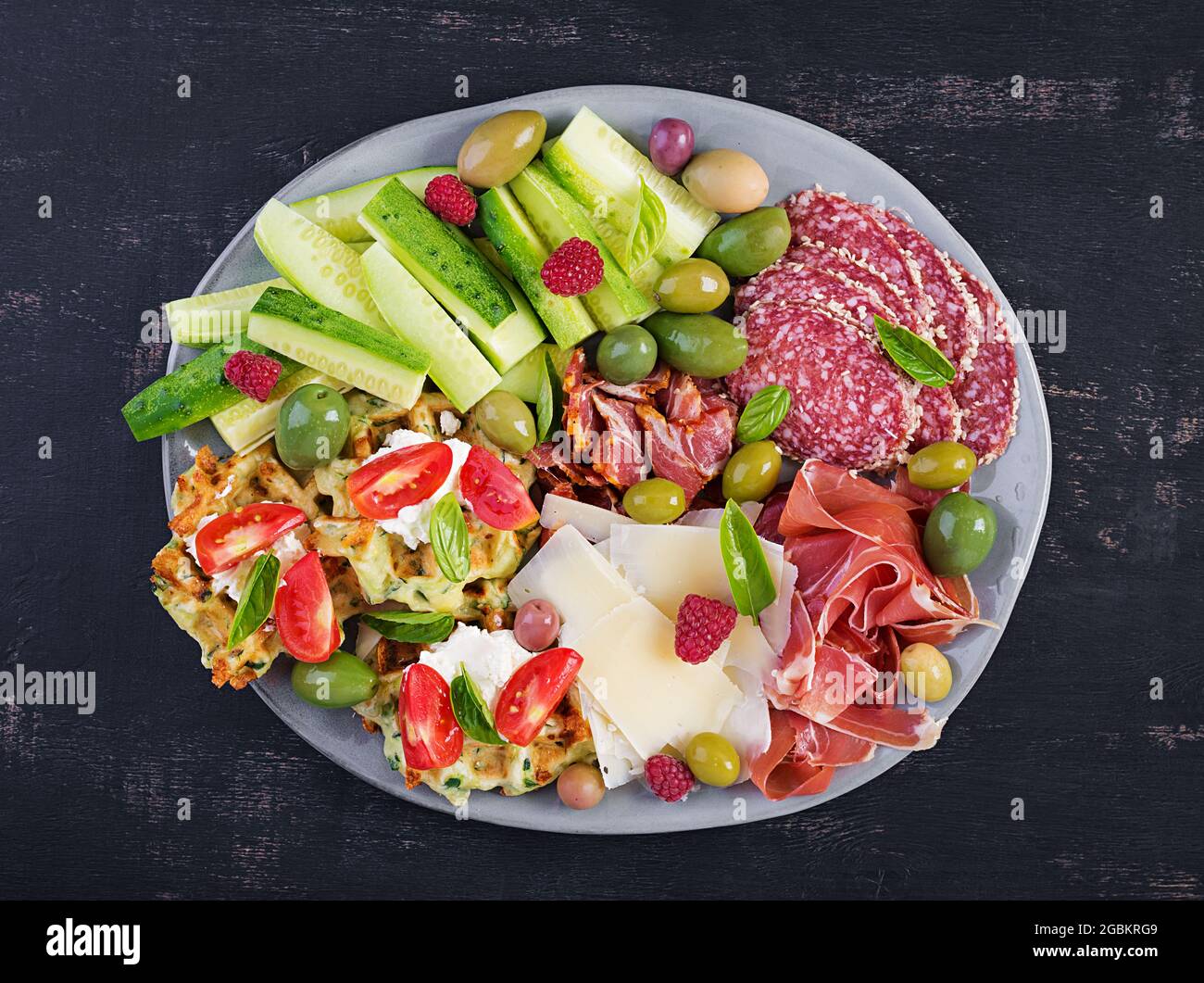 Lavagna di salumi. Piatto: parmigiano con prosciutto, salame, cetrioli e olive. Assortimento di gustosi antipasti o antipasti. Vista dall'alto, spazio di copia, Foto Stock