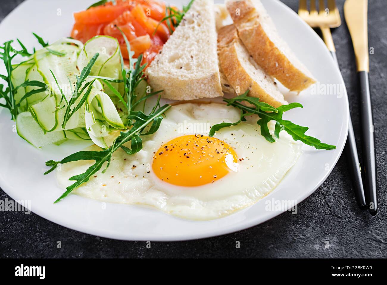 Prima colazione dietetica. Insalata di salmoni con verdure, cetrioli, uova fritte e pane. Foto Stock