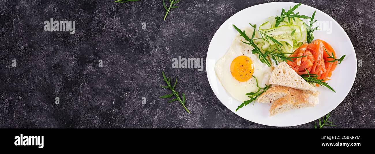 Prima colazione dietetica. Insalata di salmoni con verdure, cetrioli, uova fritte e pane. Vista dall'alto, dall'alto, banner Foto Stock