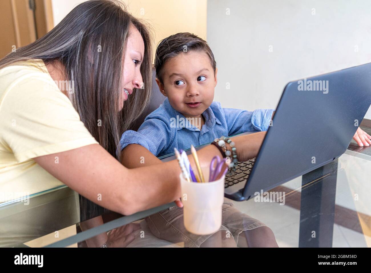 Ragazzo guarda con attenzione sua madre che lo aiuta con un lavoro su un computer portatile Foto Stock