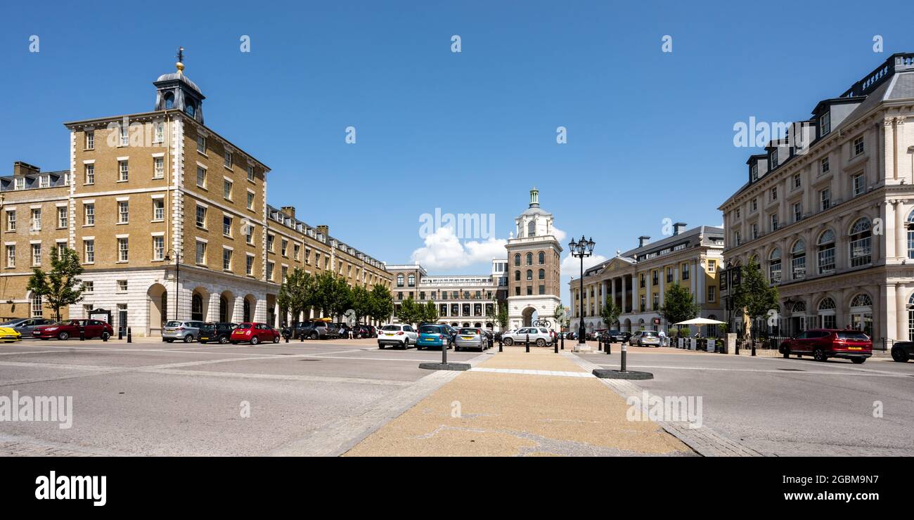 Edifici di appartamenti a uso misto di nuova costruzione, tra cui un pub e un supermercato, circondano un parcheggio presso Queen Mother Square nella nuova città di Poundbury, Dorset. Foto Stock