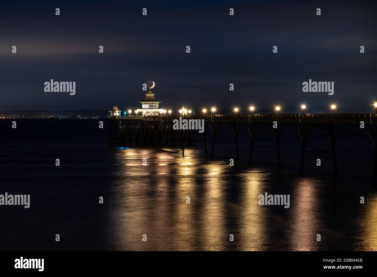 Una luna a mezzaluna si tramonta sul canale di Bristol e sul molo di Clevedon a Somerset, Inghilterra. Foto Stock